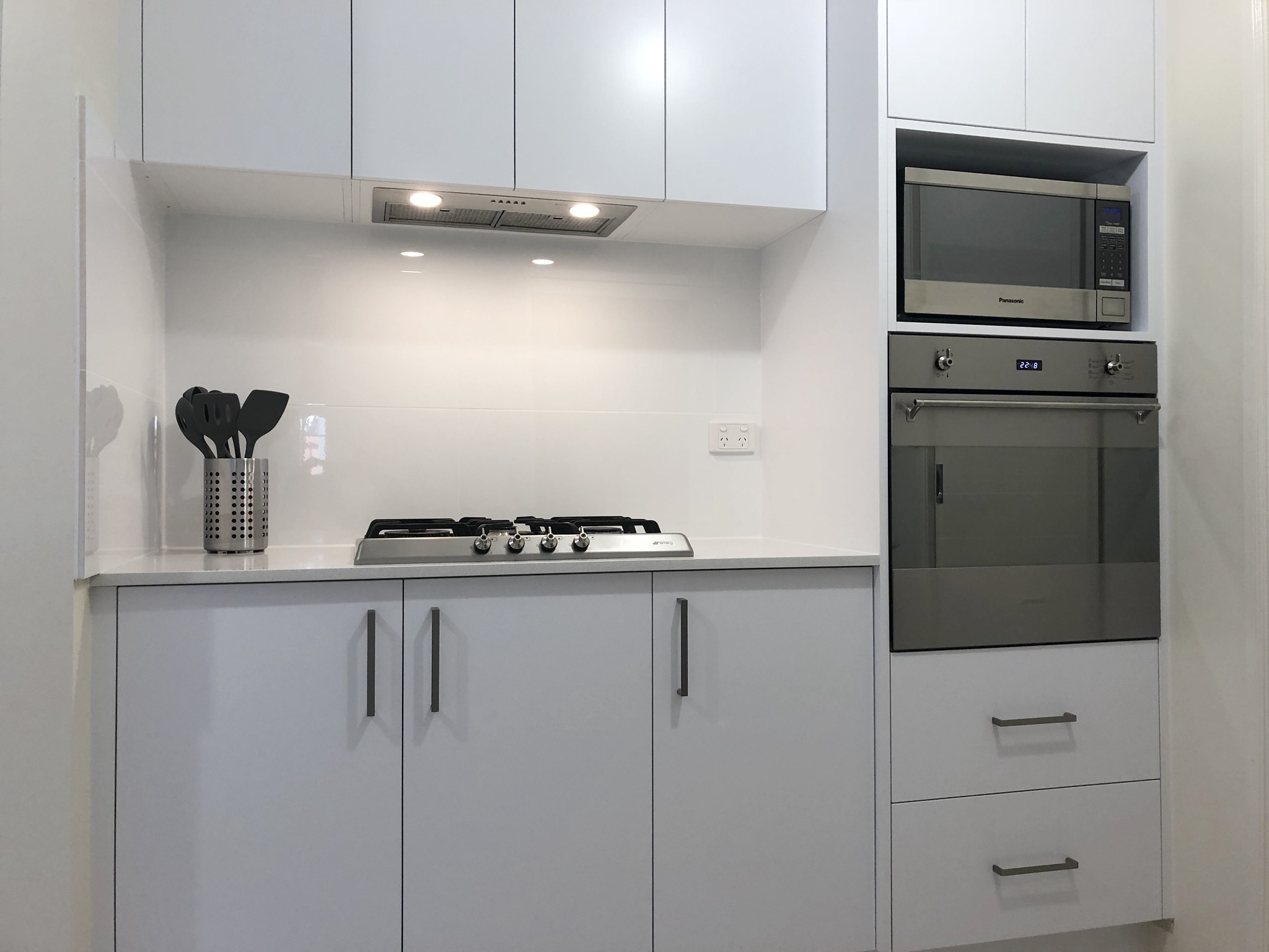 Stainless steel gas cooktop and extractor fan, wall oven and microwave with tiled splashback.