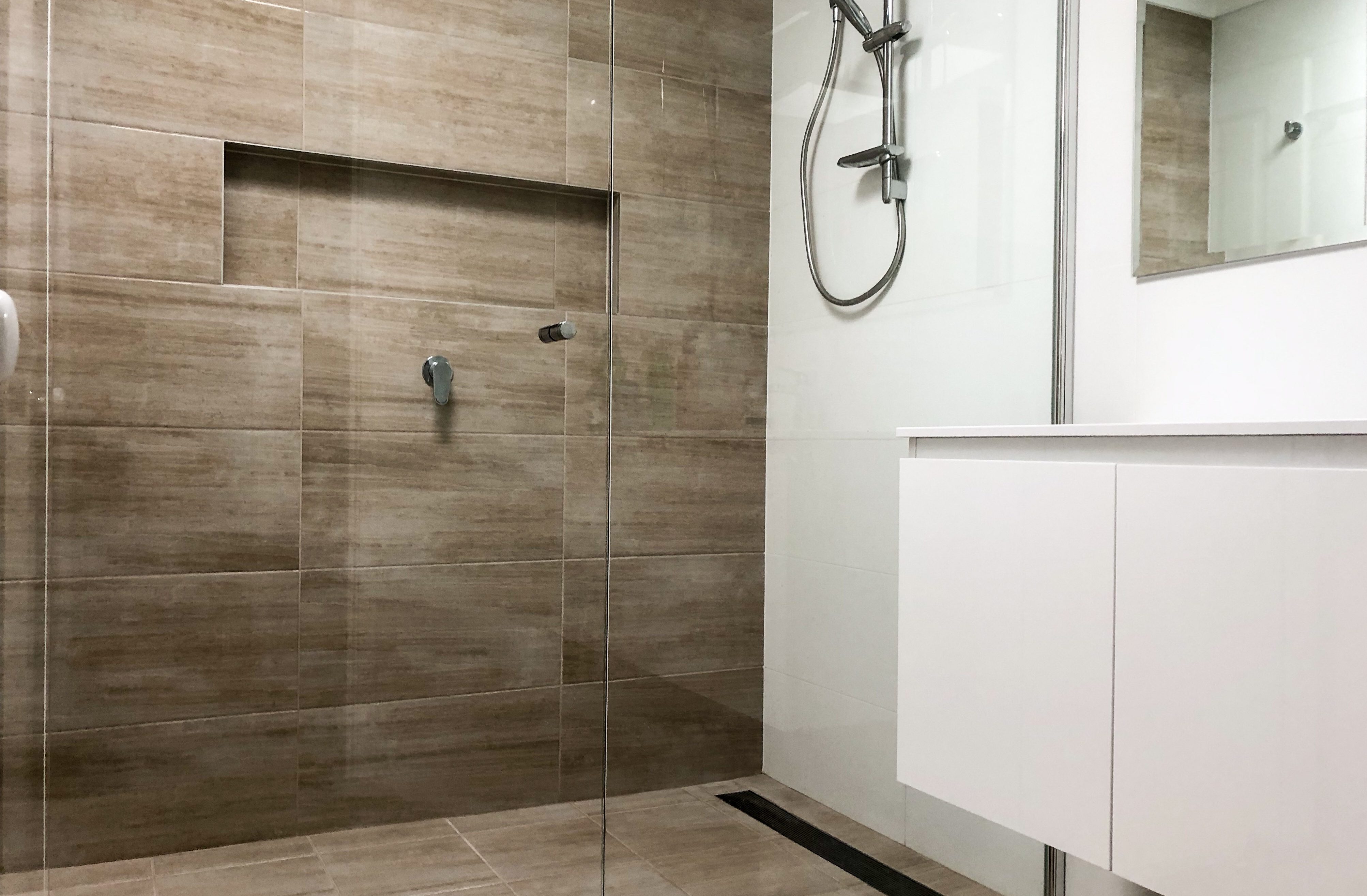 Beautiful shower recess with timber tile feature wall, shower niche, linear shower grate and semi-frameless shower screen - bathroom renovation by Master Bathrooms & Kitchens.