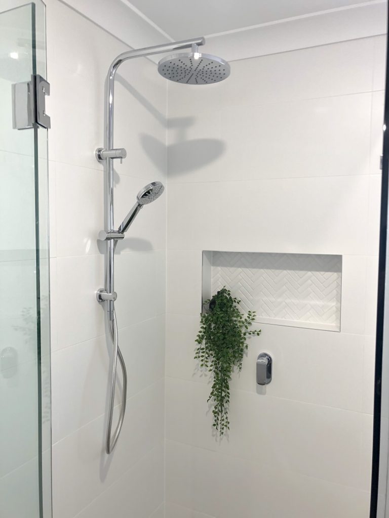 Gorgeous chrome rail shower with rainfall shower head, adjustable hand held shower rose, niche with herringbone tile, linear grate and frameless shower screen - bathroom renovation by Master Bathrooms & Kitchens.