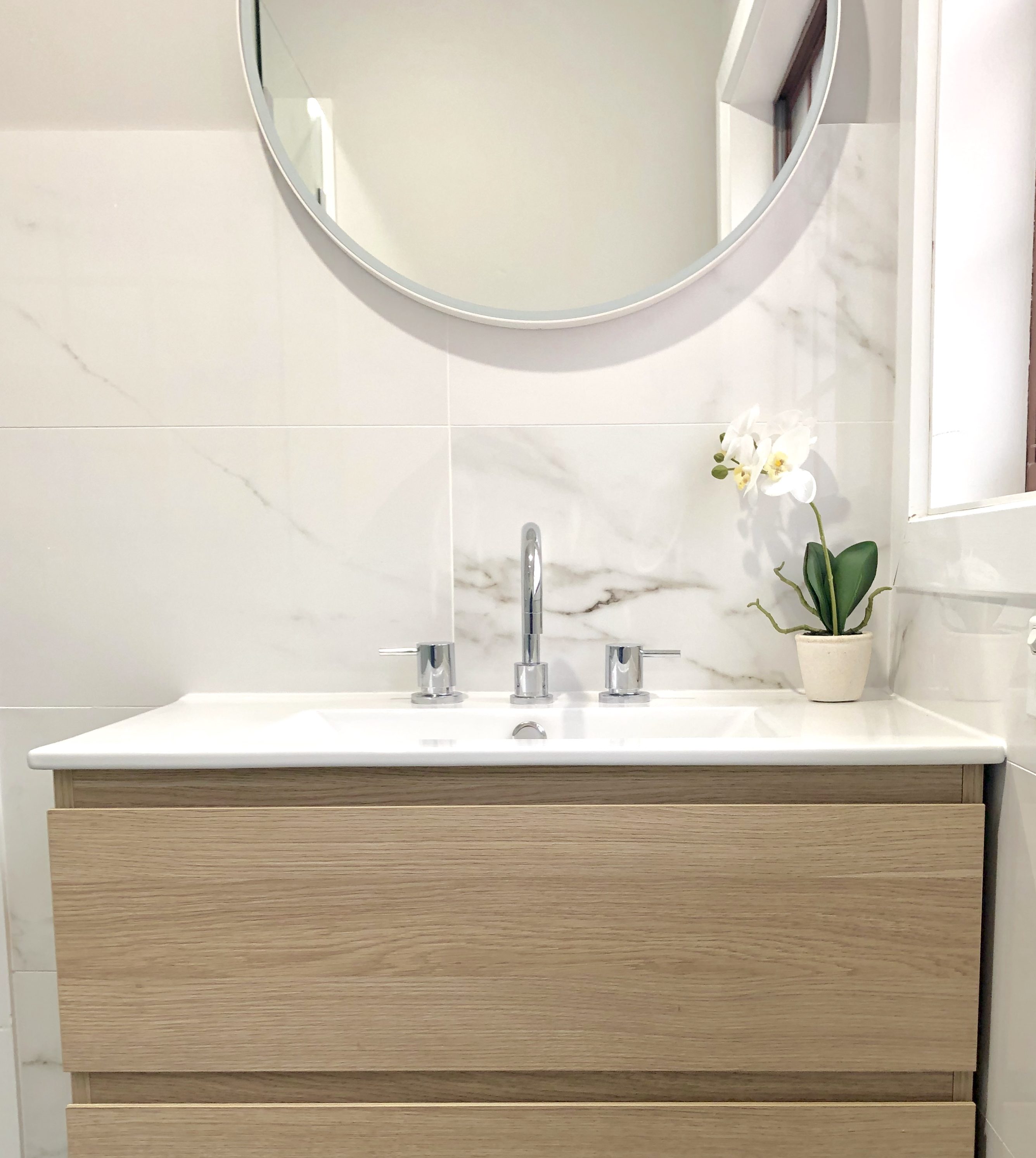 Gorgeous faux marble tiles with timber wall hung vanity and round mirror - bathroom renovation by Master Bathrooms & Kitchens.