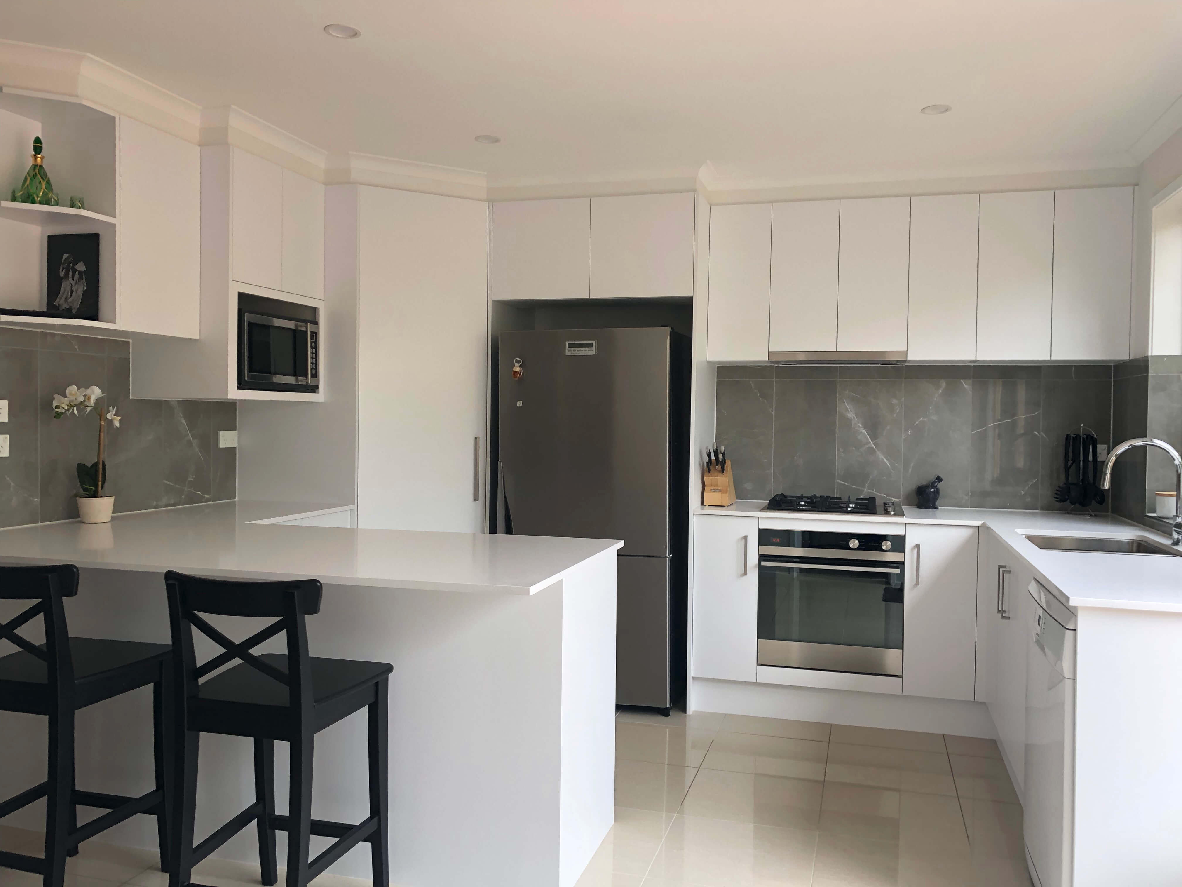 Stunning white acrylic cabinets with Caesarstone benchtops, tiled splashback and stainless steel appliances- kitchen renovation by Master Bathrooms & Kitchens.