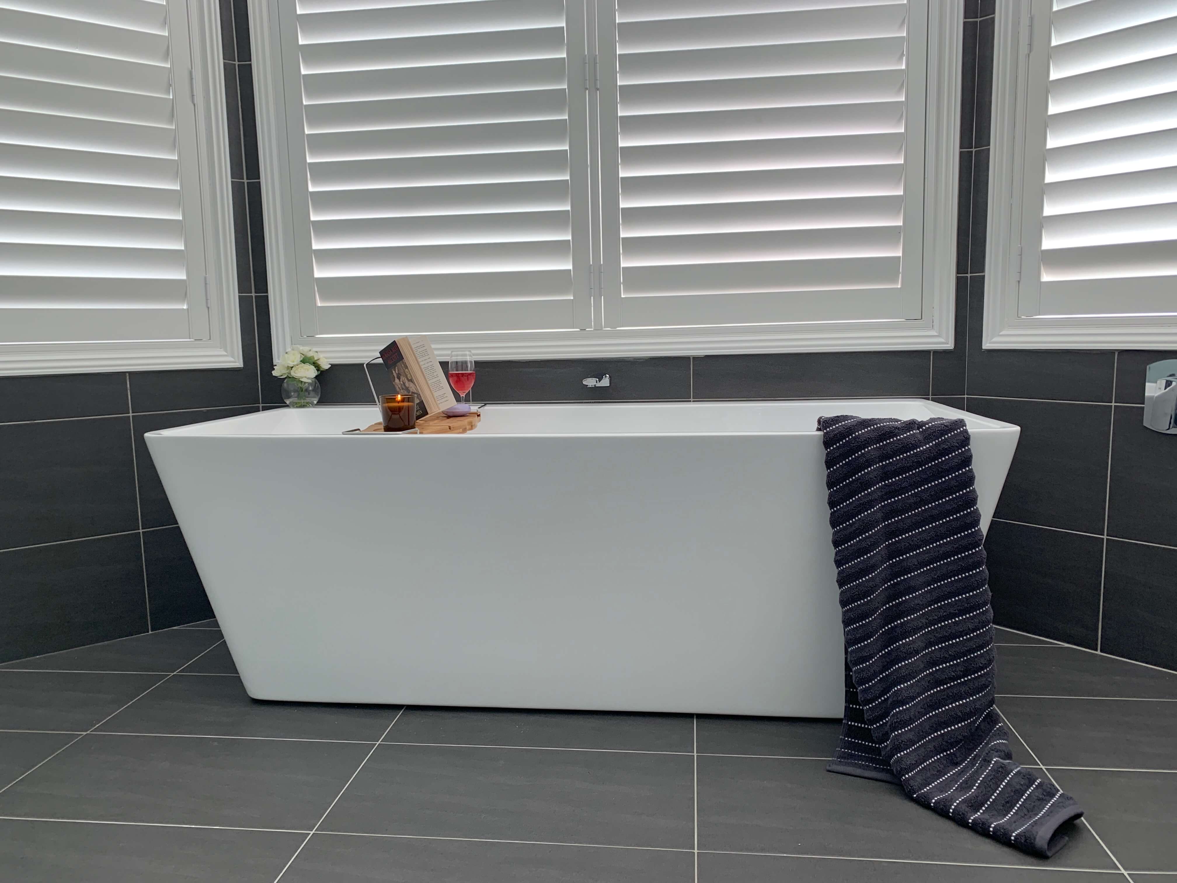 Stunning white back to wall free standing bath contrasting perfectly with the dark porcelain tiles - bathroom renovation by Master Bathrooms & Kitchens.